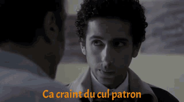 a man with curly hair talks to another man with the words ca craint du cul patron below him