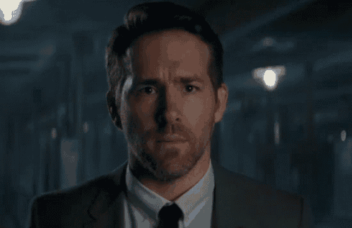 a man in a suit and blue shirt is looking up at the sky in a dark room .
