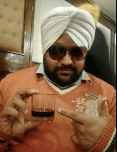 a man wearing a turban and sunglasses is holding a glass of liquid