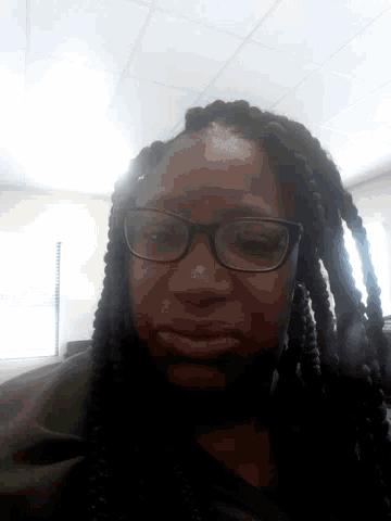 a woman wearing braids and glasses looks down at the camera