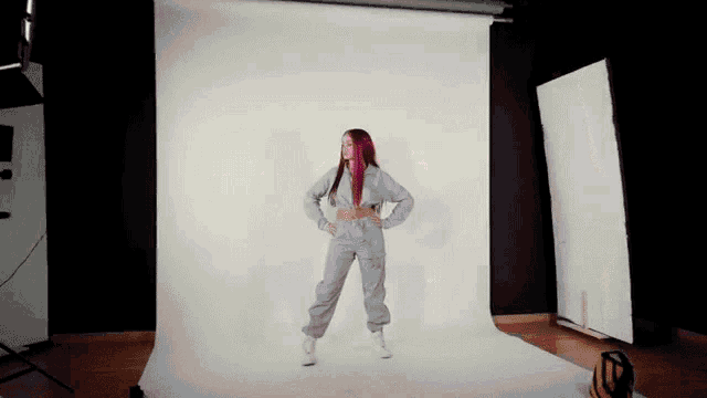 a woman in a grey jumpsuit is standing in front of a white backdrop