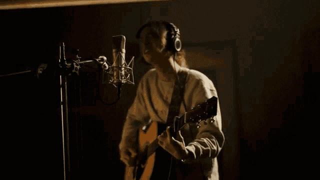 a man is playing an acoustic guitar in front of a microphone in a recording studio .
