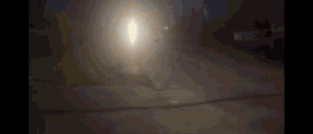 a car is driving down a street at night with a bright light shining through the fog