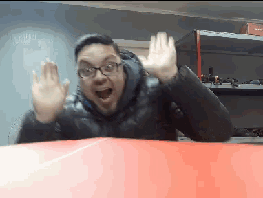 a man wearing glasses and a black jacket is waving his hands