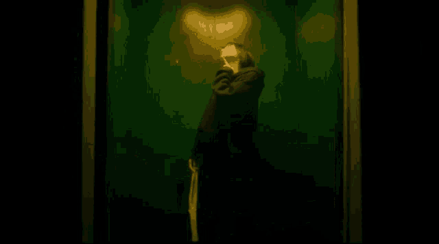 a woman in a black coat is standing in a dark room with a green wall .