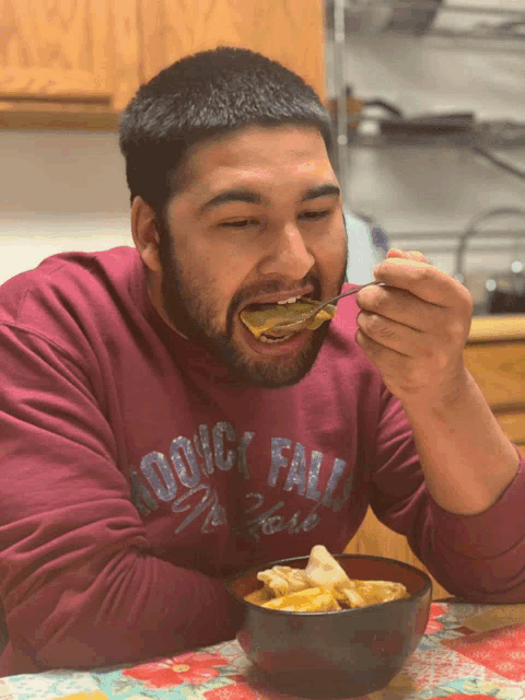 a man wearing a woody falls sweatshirt eats from a bowl of food