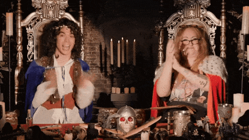 a man and a woman are sitting on a throne with candles and a skull on the table