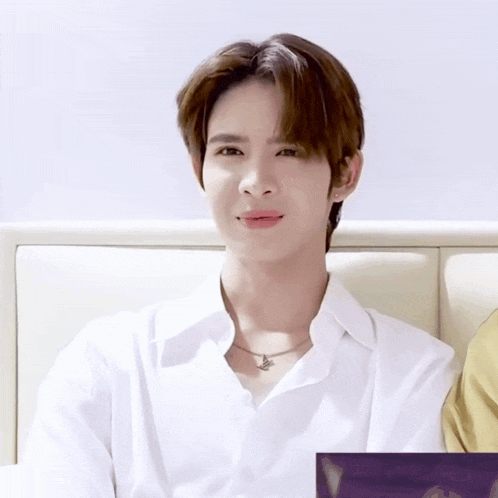 a young man wearing a white shirt and a necklace is sitting on a couch