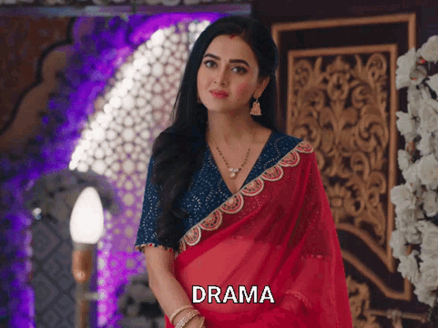 a woman in a red saree is standing in front of a wall with the word drama on it