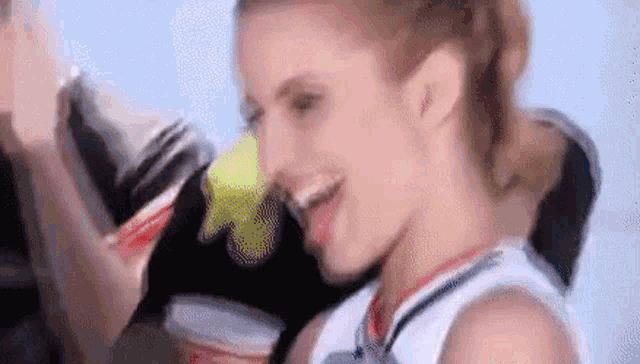a cheerleader is holding a cup of soda and smiling while standing next to a man .