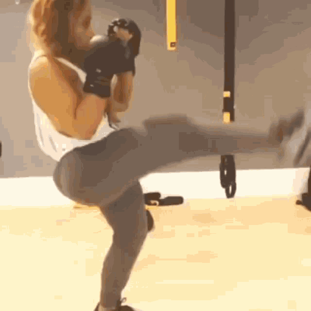 a woman is kicking her leg in the air while wearing boxing gloves in a gym .