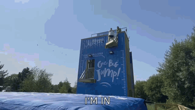 a man stands on top of a blue wall that says i 'm in