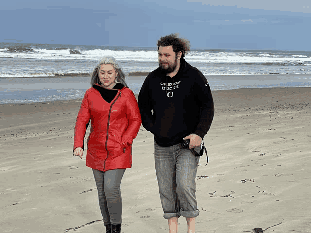 a man wearing an oregon ducks sweatshirt walks on the beach with a woman