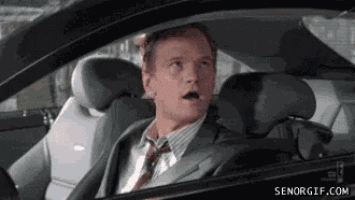 a man in a suit and tie is driving a car and looking out the window .