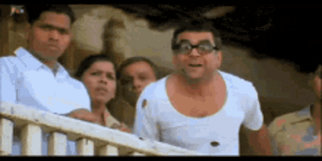 a group of people are standing on a balcony looking at a man wearing glasses .