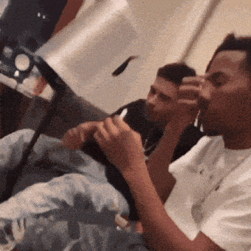 two men are sitting on a couch one is smoking a cigarette