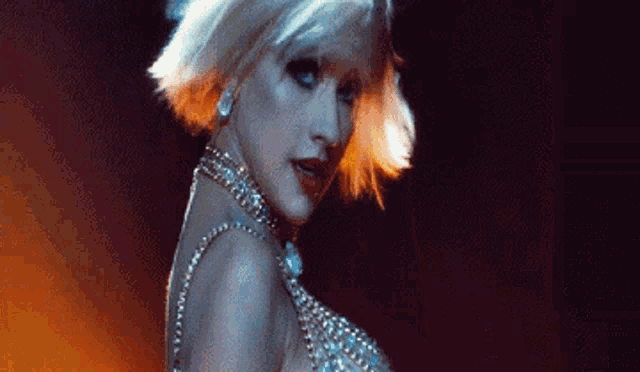 a woman with short blonde hair is wearing a necklace and earrings while dancing on a stage .