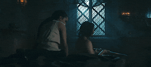 a man and woman are sitting on a bed in front of a window