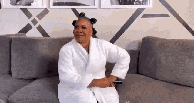 a woman in a white robe is sitting on a couch with her hair in rollers .