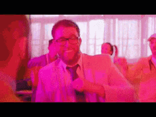 a man in a suit and tie is dancing in a room with purple lights