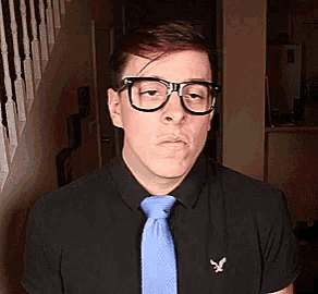 a man wearing glasses and a blue tie is standing in a hallway