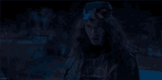 a woman with long hair and a bandana on her head is standing in a dark room .