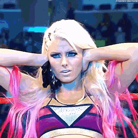 a woman with blonde hair and pink hair is sitting in a ring with her hands on her head .