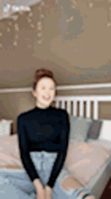 a woman is sitting on a bed wearing a black turtleneck and ripped jeans .