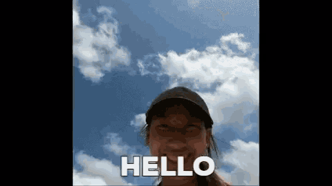 a woman in a baseball cap says hello in front of a blue sky with clouds