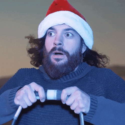 a bearded man wearing a santa hat is holding a steering wheel