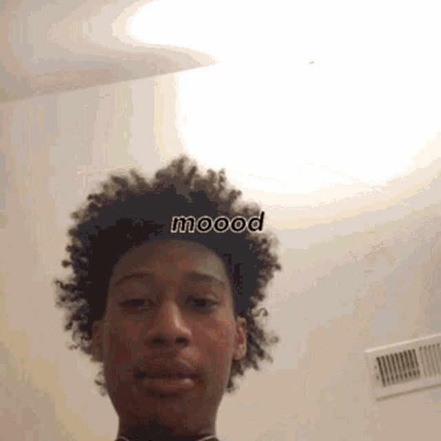 a man with curly hair is taking a selfie with the word mood on his forehead .