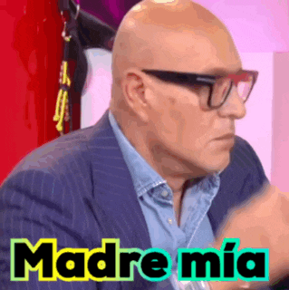 a bald man wearing glasses and a suit has the word madre mia written on his face .
