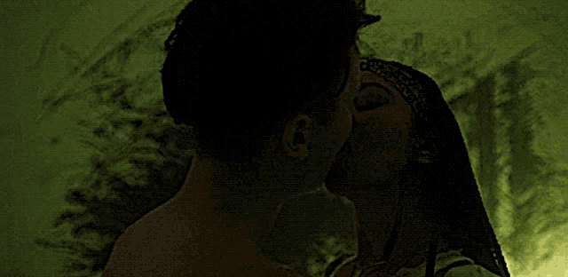 a man and woman kissing in a dark room with a green background