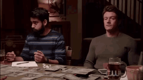 two men are sitting at a table playing a game with a glass of beer .