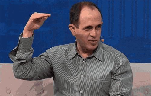 a man in a green striped shirt is sitting on a couch with his hand up