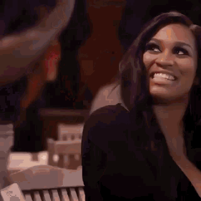 a woman in a black dress is smiling while sitting on a couch .