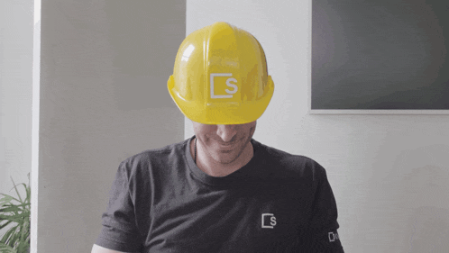 a man wearing a black shirt and a yellow hard hat with the letter s on it