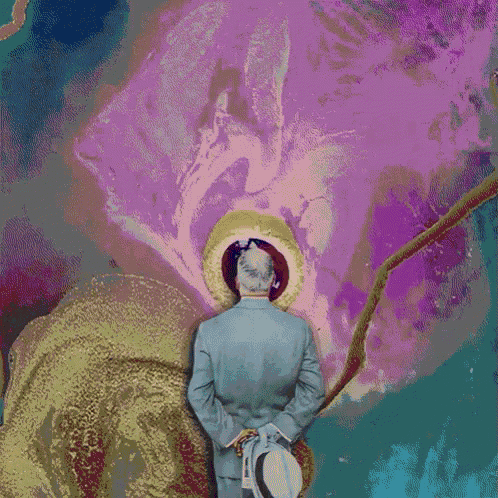 a man in a suit and hat is standing in front of a giant pink flower