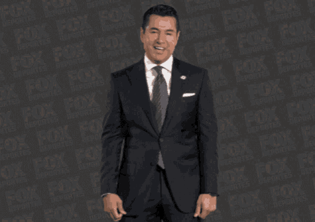 a man in a suit and tie is standing in front of a fox logo