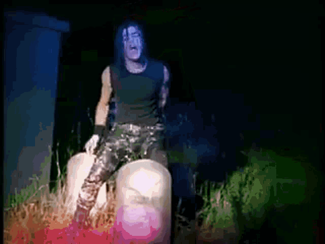 a man with long hair and a black shirt is sitting on a rock in the dark