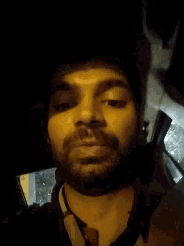 a man with a beard is smiling with his eyes closed in a dark room