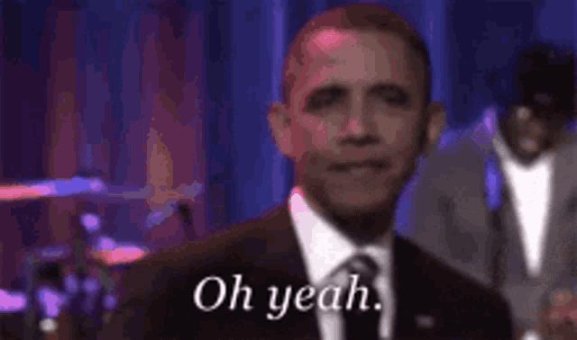 a man in a suit and tie is standing in front of a drum set and says `` oh yeah '' .