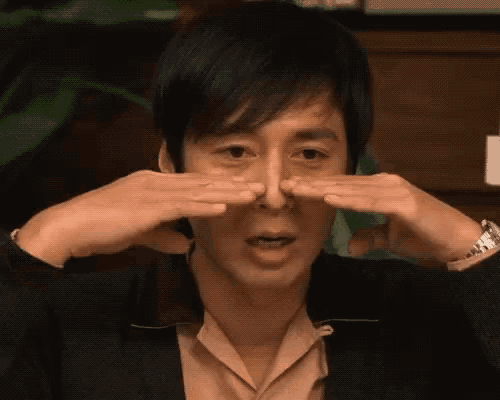 a man in a suit is holding his nose with his hands .