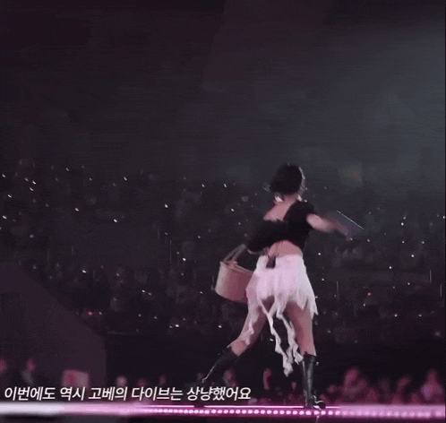 a woman in a black top and white skirt is dancing on a stage in front of a crowd
