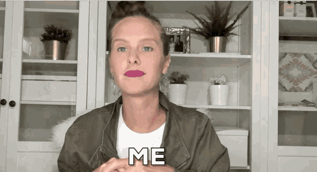 a woman in a green jacket says me in front of a shelf