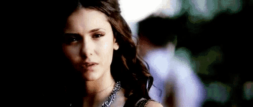 a close up of a woman 's face wearing a necklace and looking at the camera .