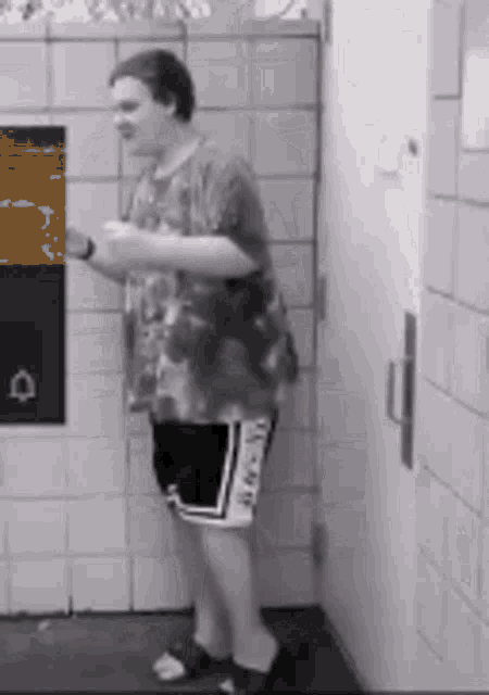 a man in a tie dye shirt and shorts is standing in front of a tiled wall .