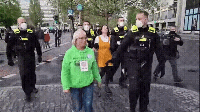 a woman in a green hoodie is being escorted by a group of police officers