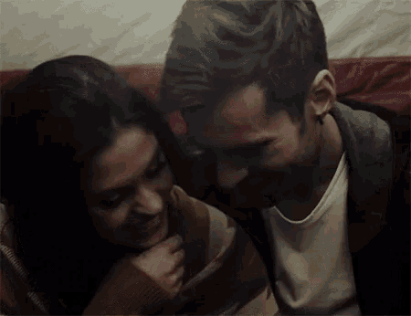 a man and a woman are sitting next to each other on a couch looking at each other .