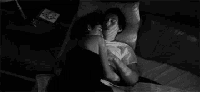 a black and white photo of a man and woman hugging each other while laying in bed .